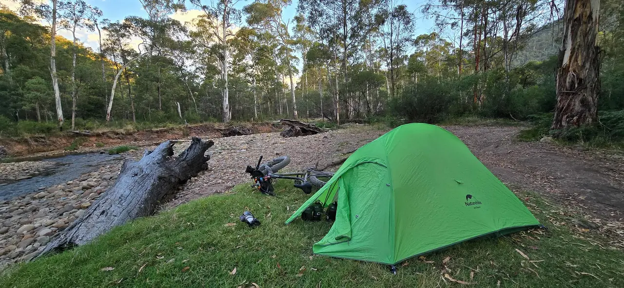 Green tent on a gravel river flat among tall gums