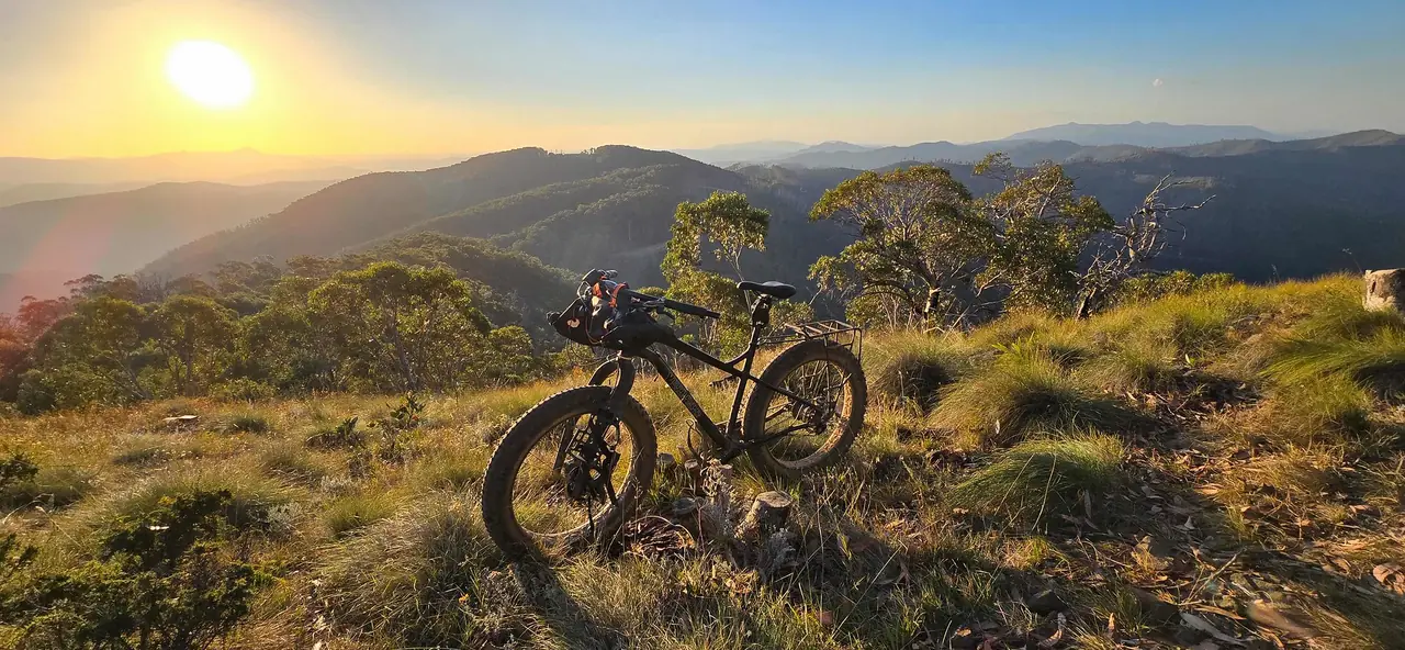 Fat bike on a grassy hilltop at sunset with ranges fading into the distance