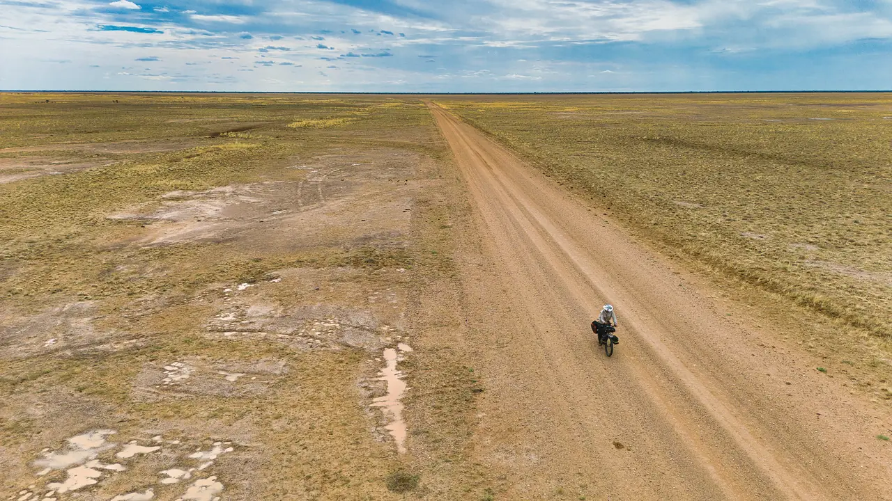 Aerial view of a lone cyclist on a straight gravel road across flat grassland