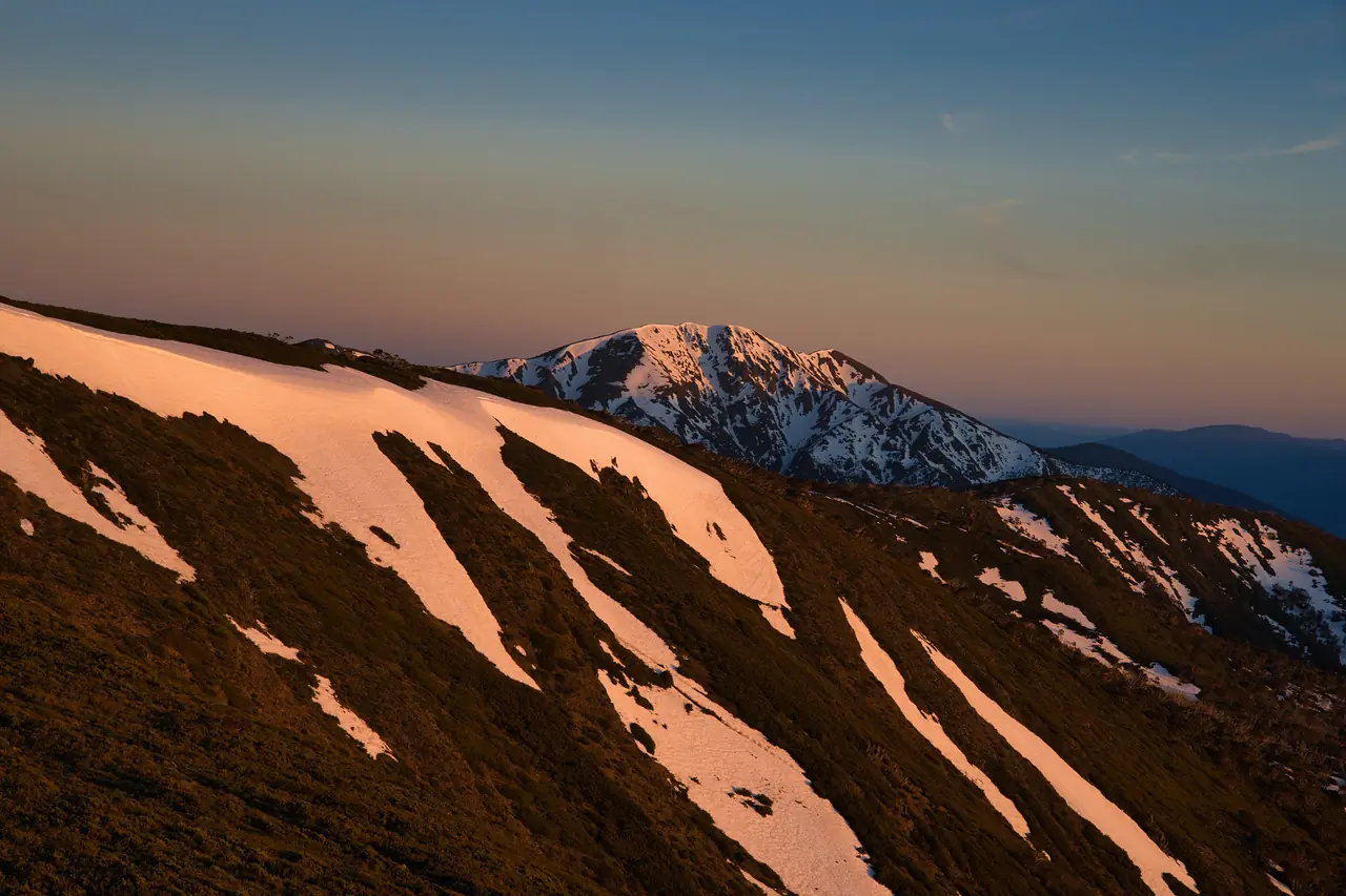 Snow patches turning pink at sunrise on a mountain ridge