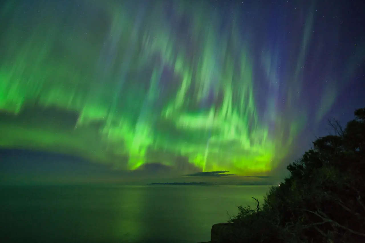 Green and violet aurora over dark sea cliffs